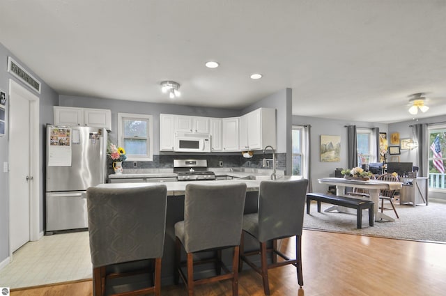 kitchen featuring stainless steel appliances, a breakfast bar, decorative backsplash, light countertops, and white cabinets