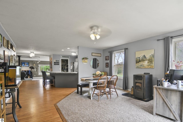 dining space featuring ceiling fan, a wood stove, baseboards, and wood finished floors