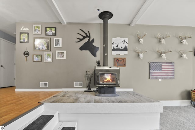 living area with a wood stove, beam ceiling, visible vents, and wood finished floors