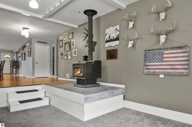 carpeted living room featuring baseboards, beamed ceiling, and a wood stove
