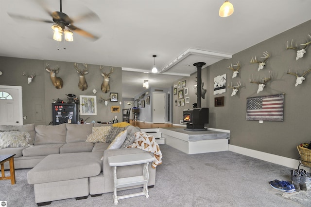 carpeted living area with a wood stove and a ceiling fan
