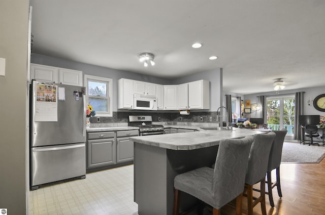 kitchen with a sink, a peninsula, stainless steel appliances, a kitchen bar, and gray cabinetry