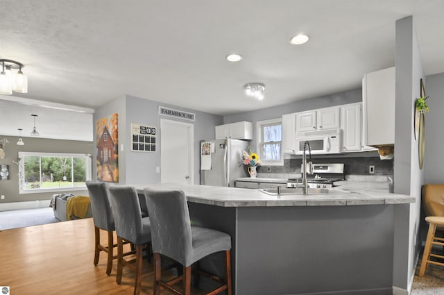kitchen with freestanding refrigerator, a peninsula, a kitchen bar, and white microwave