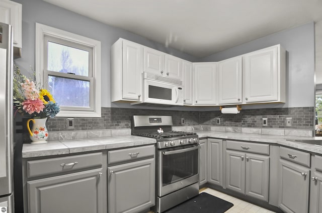 kitchen with gray cabinetry, white cabinetry, white microwave, stainless steel range with gas cooktop, and backsplash