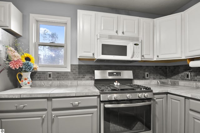 kitchen featuring stainless steel gas range oven, white cabinets, white microwave, tasteful backsplash, and gray cabinets