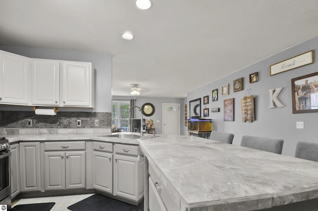 kitchen with a peninsula, a sink, white cabinets, stainless steel stove, and tasteful backsplash