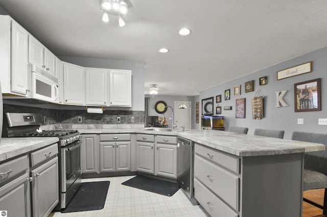 kitchen with a sink, a peninsula, gray cabinetry, and appliances with stainless steel finishes