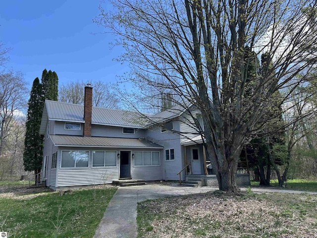 traditional home featuring a front lawn, a chimney, and metal roof