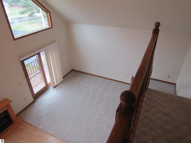 unfurnished living room with lofted ceiling, light carpet, baseboards, and plenty of natural light
