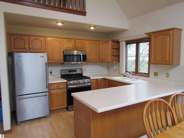 kitchen with lofted ceiling, a sink, a peninsula, tasteful backsplash, and appliances with stainless steel finishes