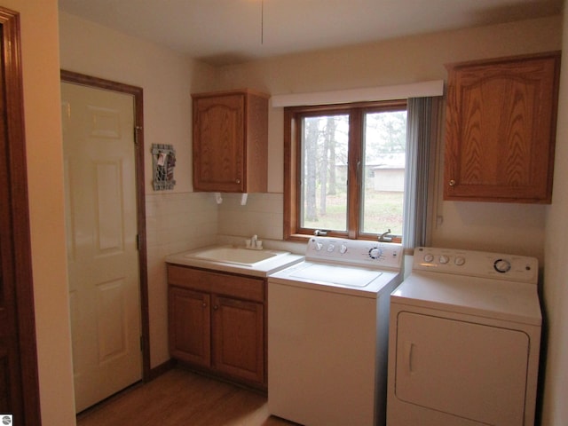 washroom featuring washing machine and clothes dryer, light wood finished floors, a sink, and cabinet space