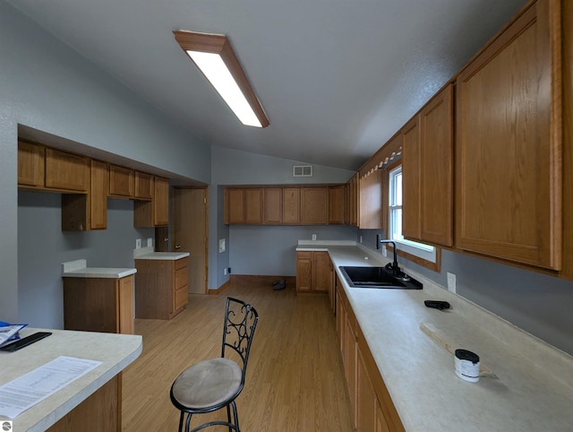 kitchen with brown cabinetry, visible vents, a sink, vaulted ceiling, and light wood-type flooring