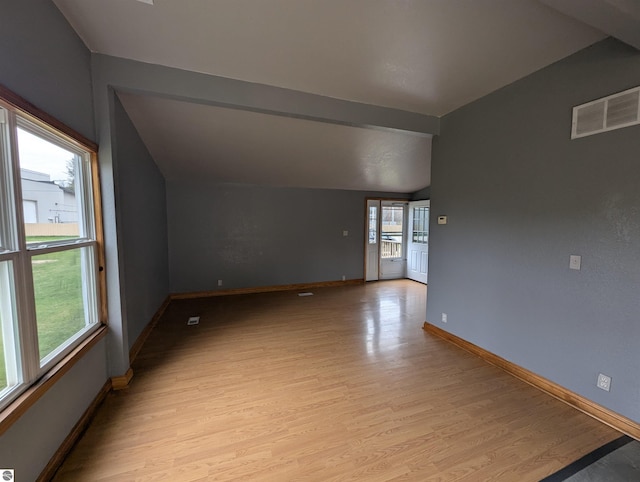 interior space featuring light wood-type flooring, baseboards, visible vents, and vaulted ceiling