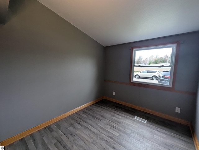 empty room featuring baseboards, visible vents, wood finished floors, and lofted ceiling