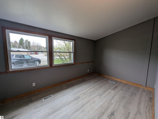 empty room featuring baseboards, light wood finished floors, visible vents, and vaulted ceiling