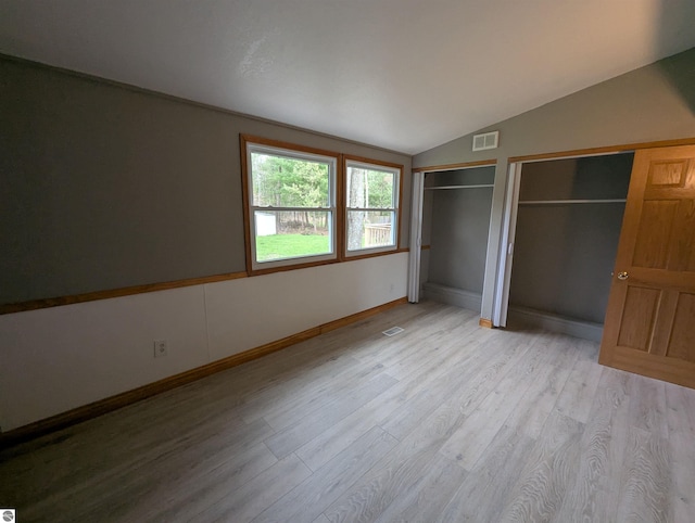 unfurnished bedroom with wood finished floors, two closets, visible vents, baseboards, and vaulted ceiling