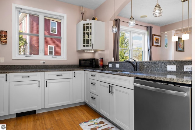 kitchen featuring glass insert cabinets, dark stone countertops, stainless steel dishwasher, decorative light fixtures, and light wood-style floors
