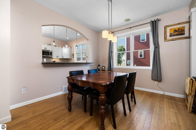 dining room featuring baseboards, light wood-type flooring, and arched walkways