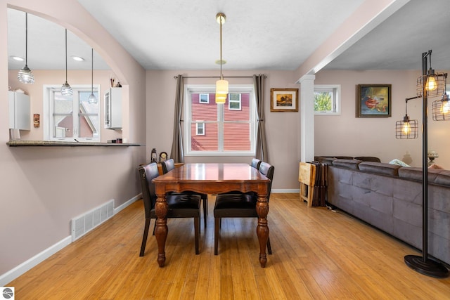 dining area featuring light wood finished floors, baseboards, visible vents, and decorative columns