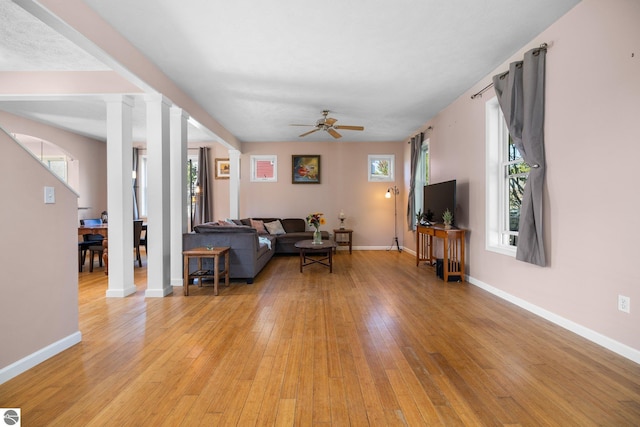 living area featuring baseboards, light wood-style flooring, decorative columns, and ceiling fan