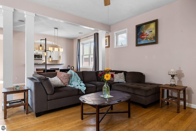 living area with baseboards, light wood-type flooring, and decorative columns