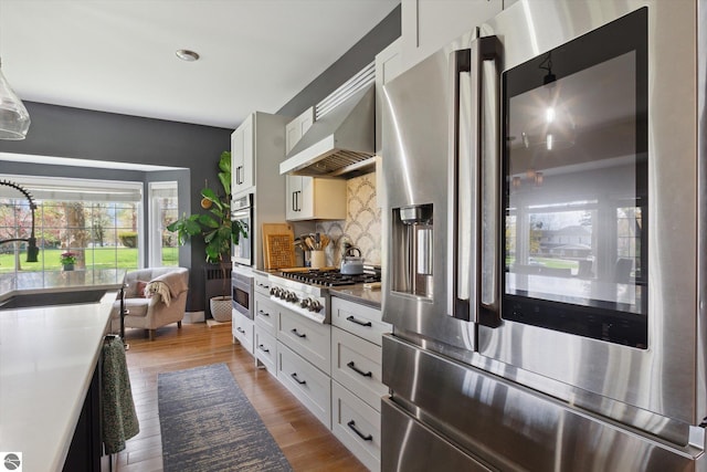 kitchen with a sink, white cabinets, under cabinet range hood, appliances with stainless steel finishes, and tasteful backsplash