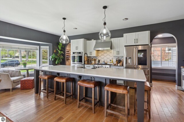 kitchen featuring range hood, a sink, backsplash, light wood-style floors, and appliances with stainless steel finishes