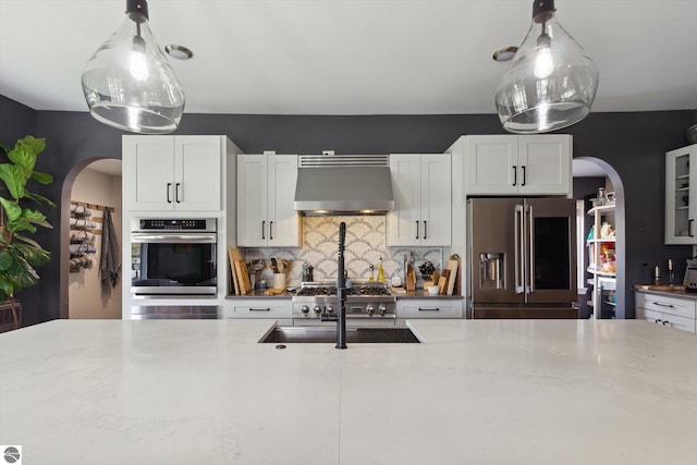 kitchen with backsplash, appliances with stainless steel finishes, arched walkways, and wall chimney exhaust hood