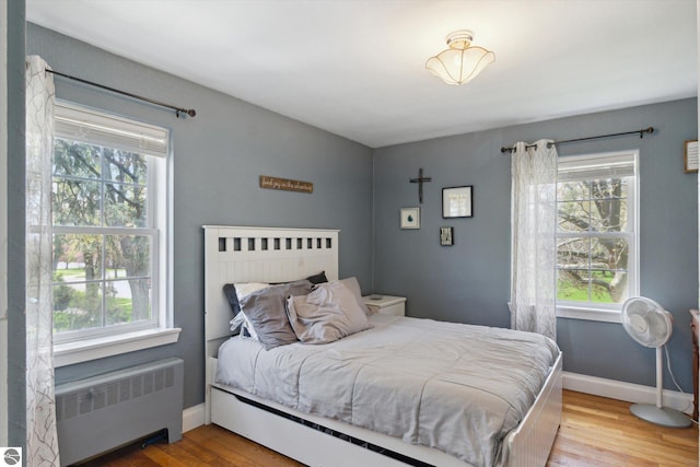 bedroom featuring wood finished floors, multiple windows, and radiator heating unit