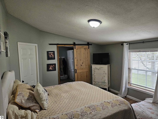 bedroom featuring wood finished floors, vaulted ceiling, a barn door, and a textured ceiling
