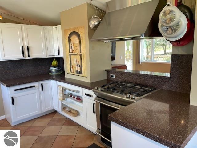 3312 Zimmerman Rd, Traverse City, MI 49685 - kitchen with wall chimney exhaust hood, gas stove, a peninsula, light tile patterned floors, and white cabinetry