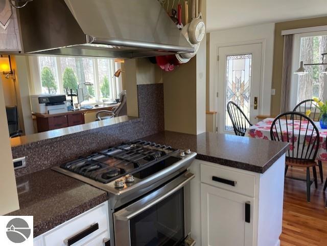 3312 Zimmerman Rd, Traverse City, MI 49685 - kitchen featuring stainless steel range with gas cooktop, exhaust hood, white cabinetry, dark countertops, and a peninsula