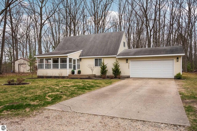 7555 Anthony St, Fife Lake, MI 49633 - view of front facade featuring a sunroom, a garage, concrete driveway, a shingled roof, and a front yard