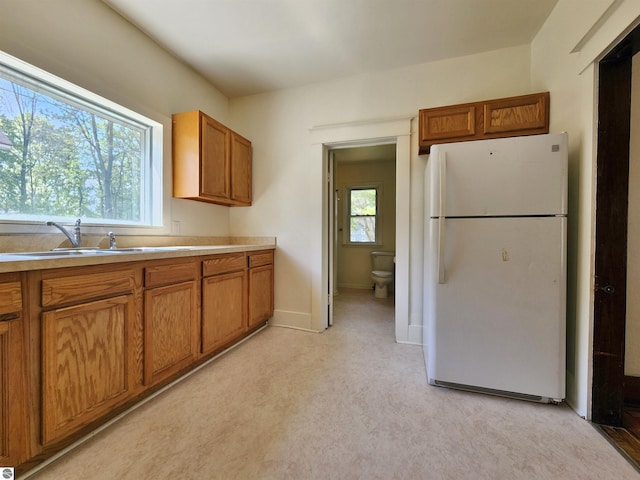 kitchen with freestanding refrigerator, brown cabinets, a sink, light countertops, and baseboards