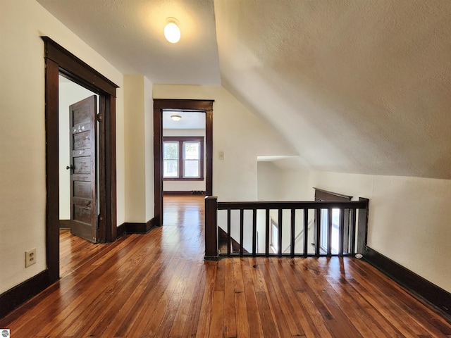 bonus room with wood-type flooring, a textured ceiling, baseboards, and vaulted ceiling