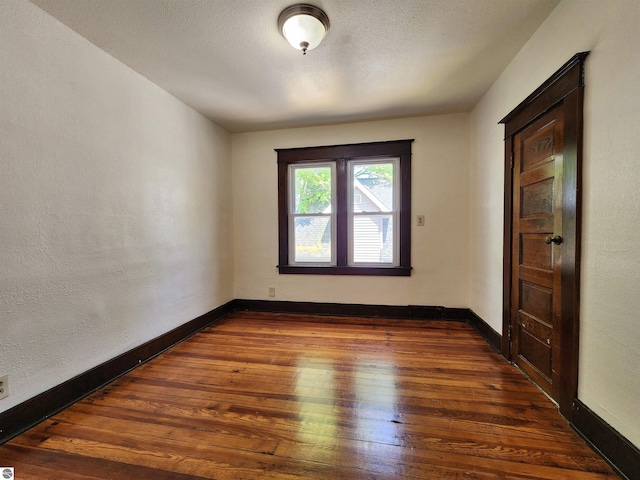 spare room featuring wood-type flooring, baseboards, and a textured wall