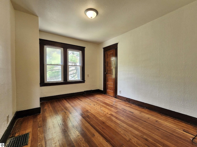 unfurnished room with hardwood / wood-style floors, baseboards, and a textured wall