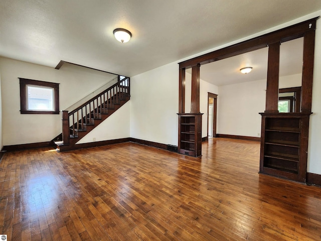 unfurnished living room with hardwood / wood-style flooring, stairs, baseboards, and decorative columns