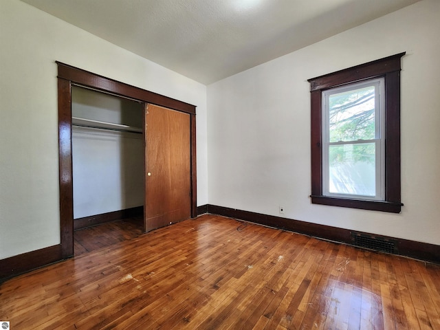 unfurnished bedroom featuring wood-type flooring, baseboards, and a closet