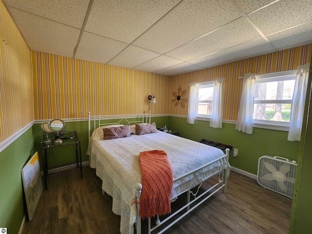bedroom featuring a paneled ceiling, wood finished floors, baseboards, and wallpapered walls