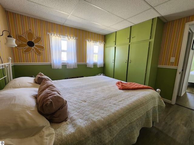 bedroom with wood finished floors, wallpapered walls, a closet, a paneled ceiling, and baseboards