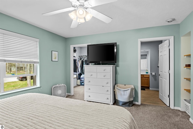 8565 Bent Pine Dr, Lake Ann, MI 49650 - carpeted bedroom featuring a walk in closet, baseboards, a closet, connected bathroom, and a ceiling fan