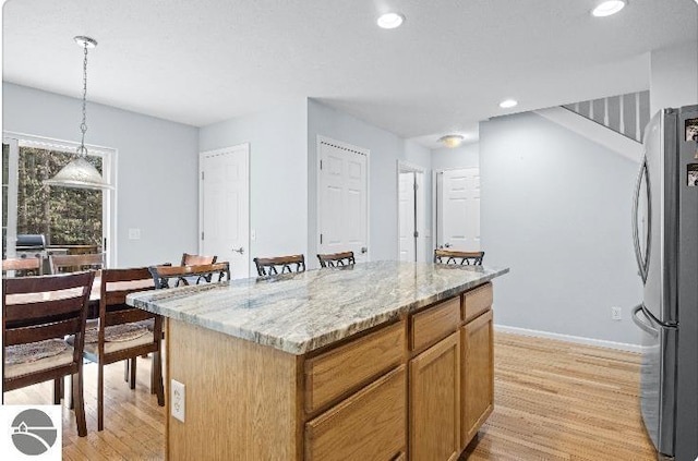 8565 Bent Pine Dr, Lake Ann, MI 49650 - kitchen featuring freestanding refrigerator, light wood-style floors, light stone counters, pendant lighting, and a center island