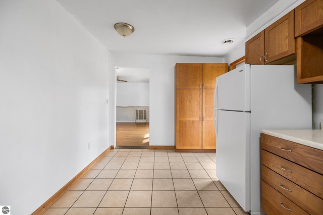 kitchen featuring brown cabinets, freestanding refrigerator, baseboards, and light countertops