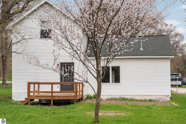 back of house with a lawn, a wooden deck, and roof with shingles