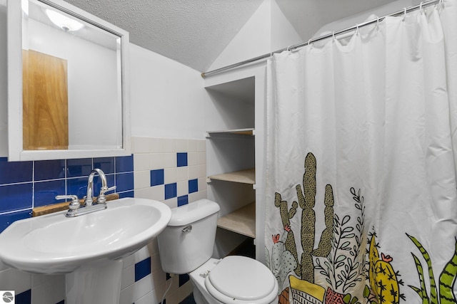 bathroom with a sink, toilet, tile walls, wainscoting, and a textured ceiling