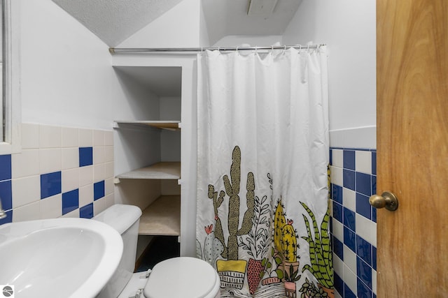 bathroom featuring tile walls, a sink, wainscoting, toilet, and a shower with shower curtain