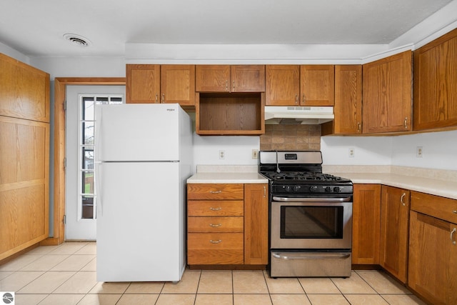kitchen with stainless steel gas stove, freestanding refrigerator, under cabinet range hood, and brown cabinets