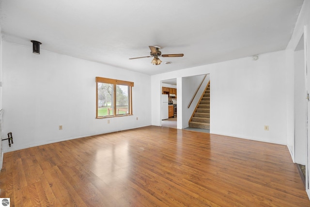 unfurnished living room with ceiling fan, stairs, and wood finished floors