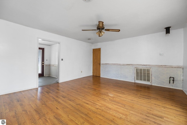 empty room featuring ceiling fan, wood finished floors, and a wainscoted wall